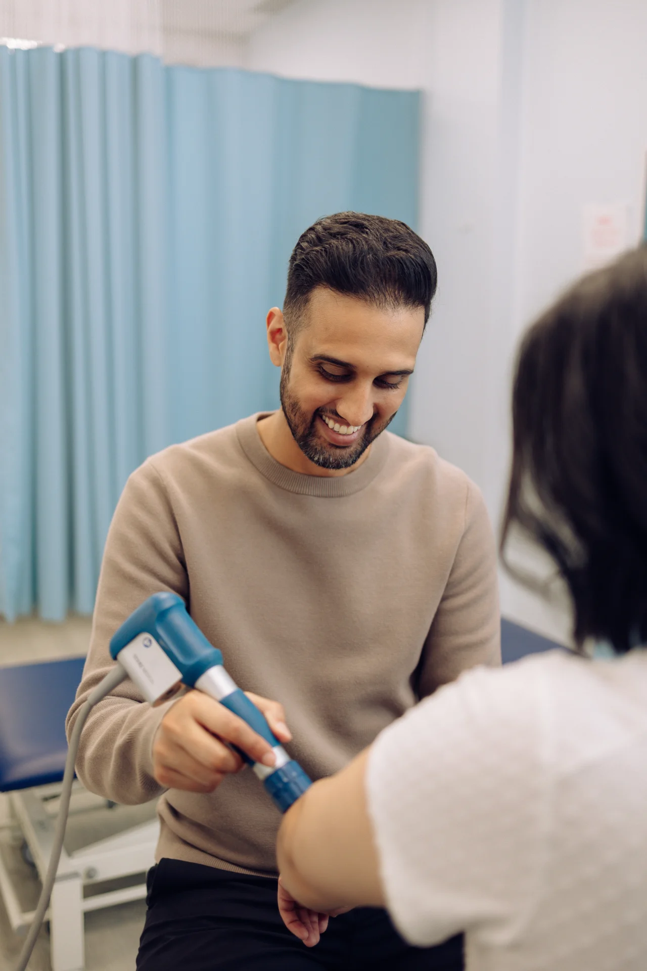 A man uses a medical device on another person's arm in a clinic setting.