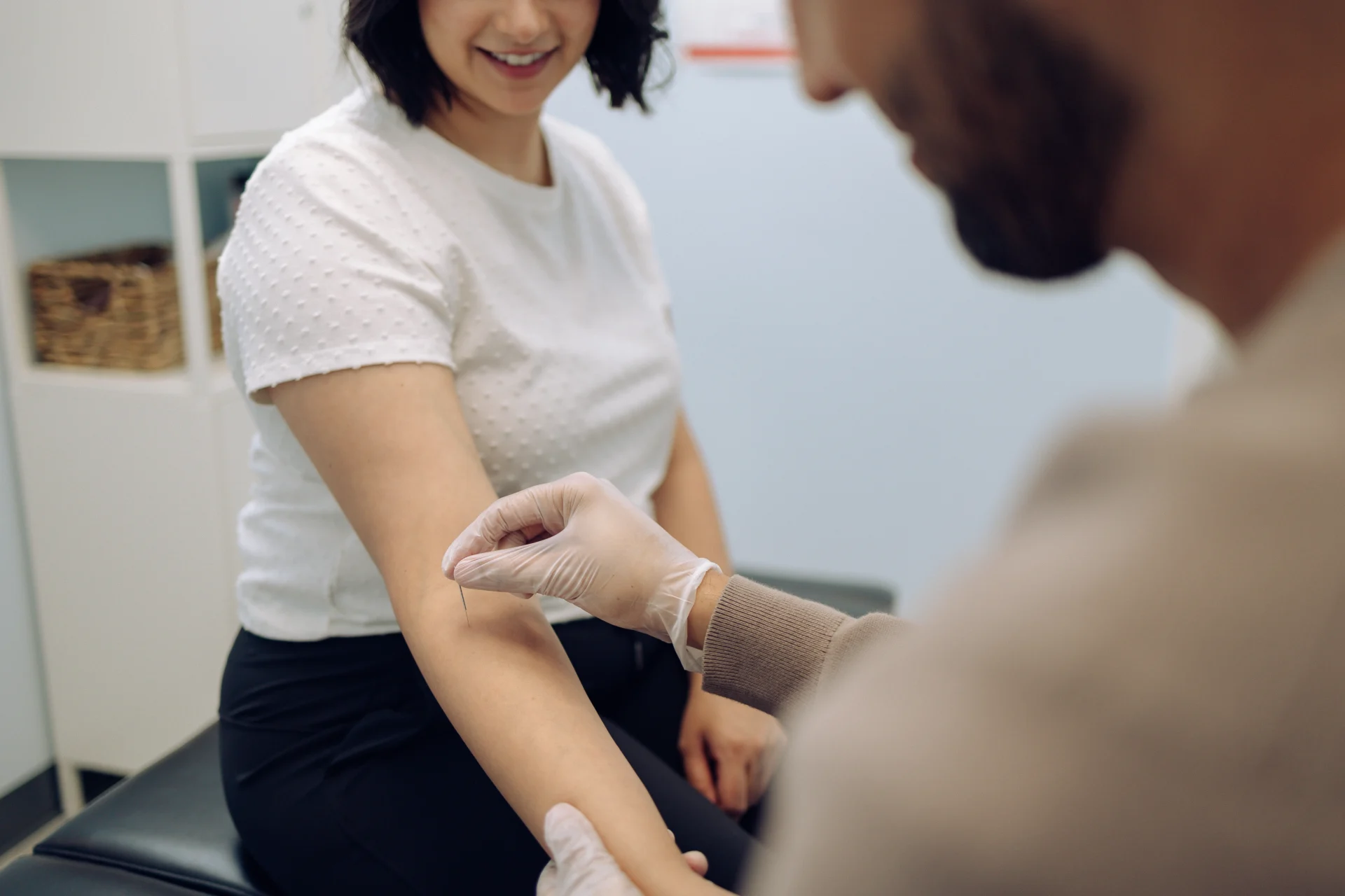 A healthcare professional applies a bandage to a patient's arm in a medical office. The patient is seated and smiling.
