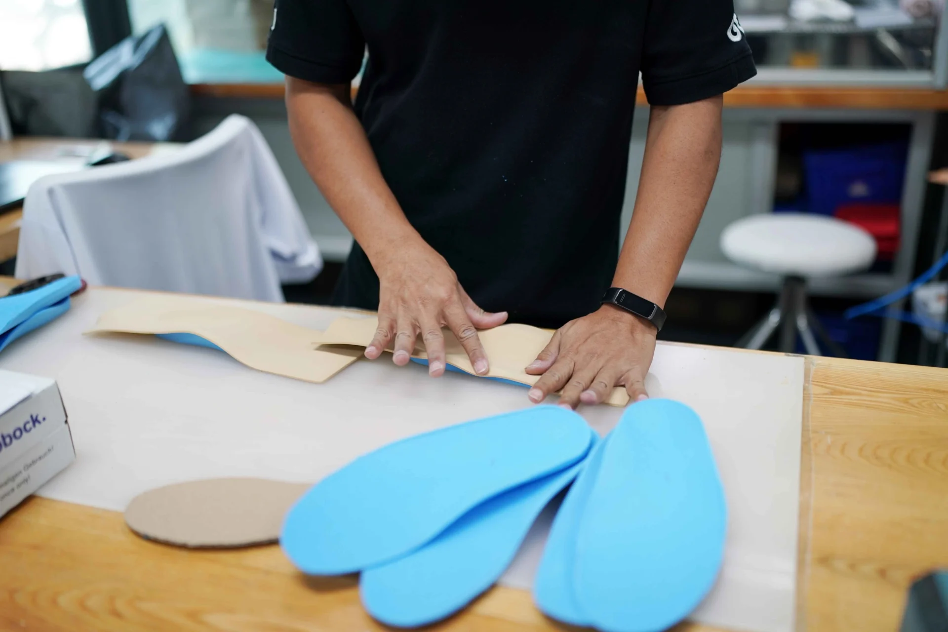 Person crafting blue insoles on a workbench, with hands positioning materials.